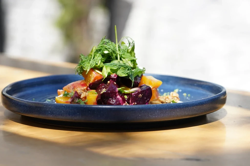Beet and orange salad topped with greens on a dark blue plate.