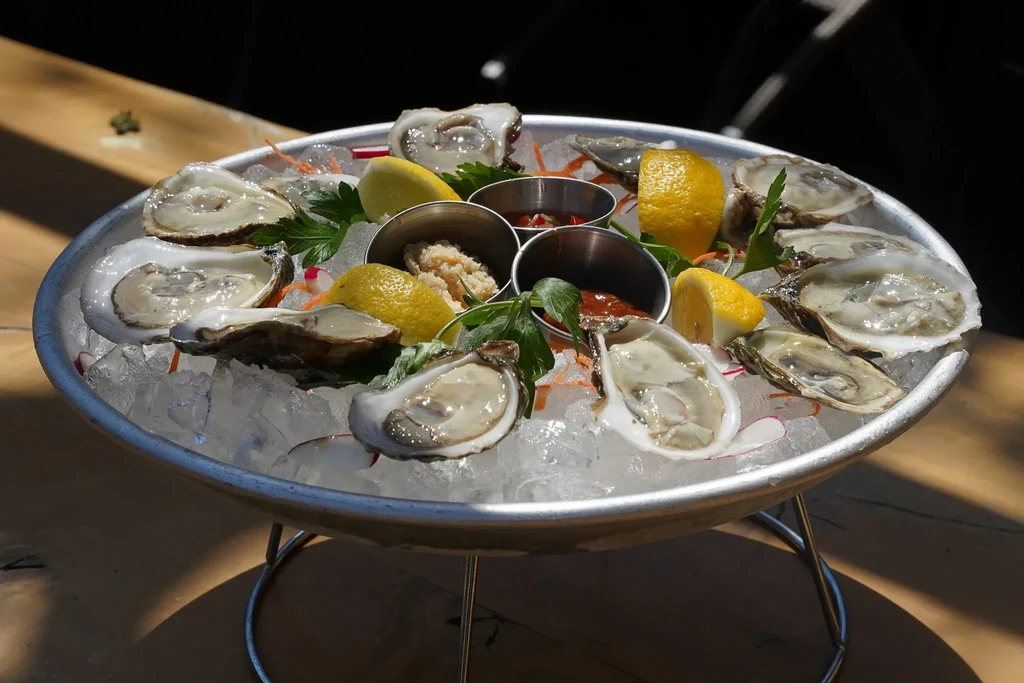A platter of fresh oysters on ice with lemon wedges and sauces.