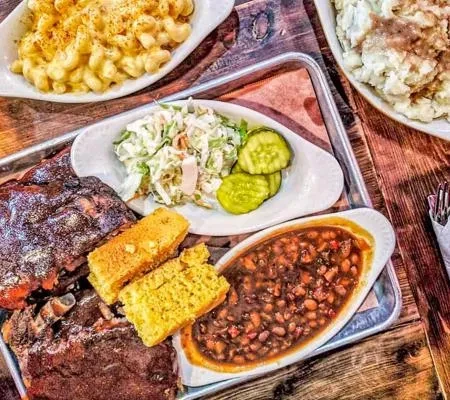 Ribs, baked beans, cornbread, and coleslaw on a metal tray.