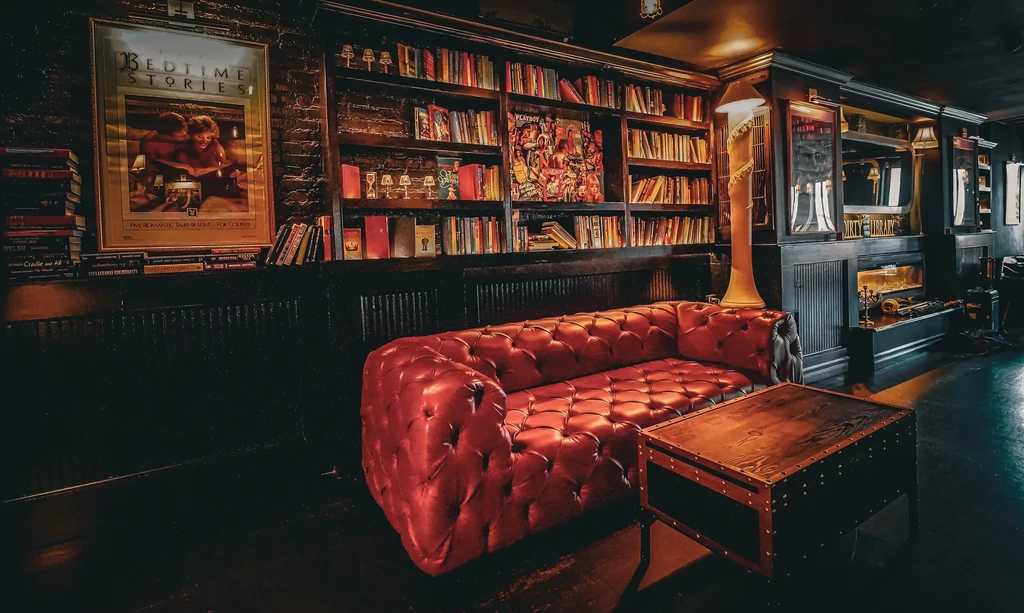 A cozy, dim-lit library with a red tufted leather sofa.