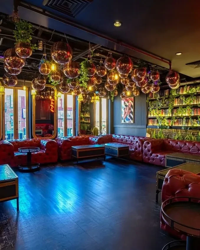 A lounge with red couches, disco balls, and plants hanging from the ceiling.