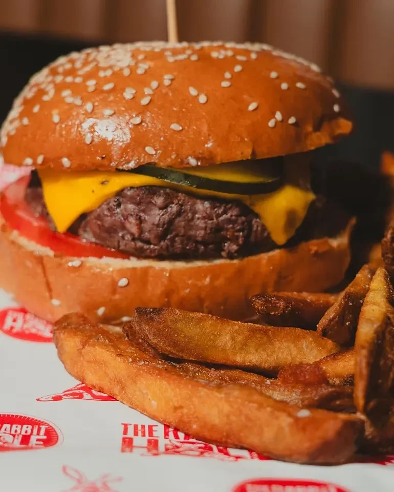 Close-up of a cheeseburger with pickles, tomato, and a side of fries.
