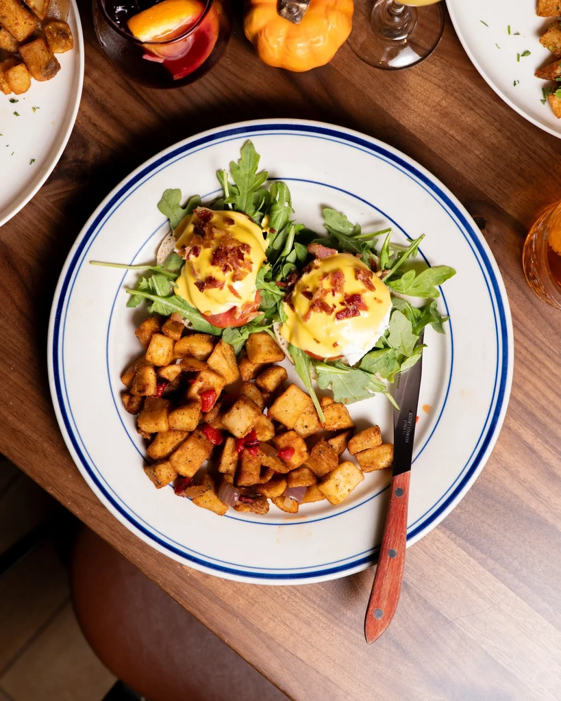 Eggs Benedict with home fries on a white plate with blue stripes.
