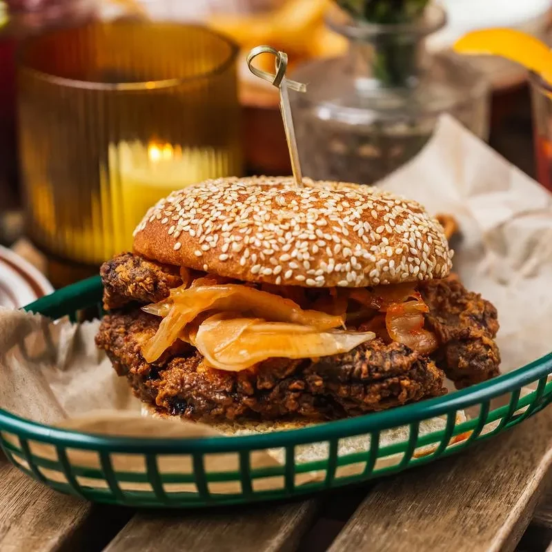 A fried chicken sandwich with pickled onions in a green basket.