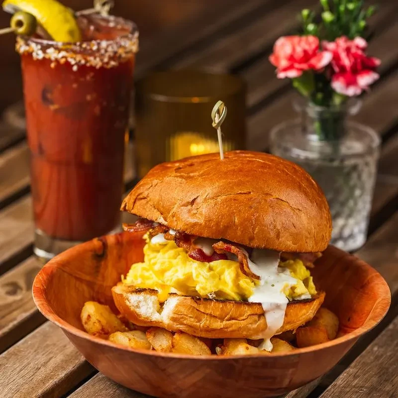 Breakfast sandwich with scrambled eggs, bacon, and sauce, served with fries.