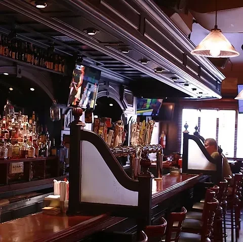 A long bar with beer taps and bottles, a person sits at the end.