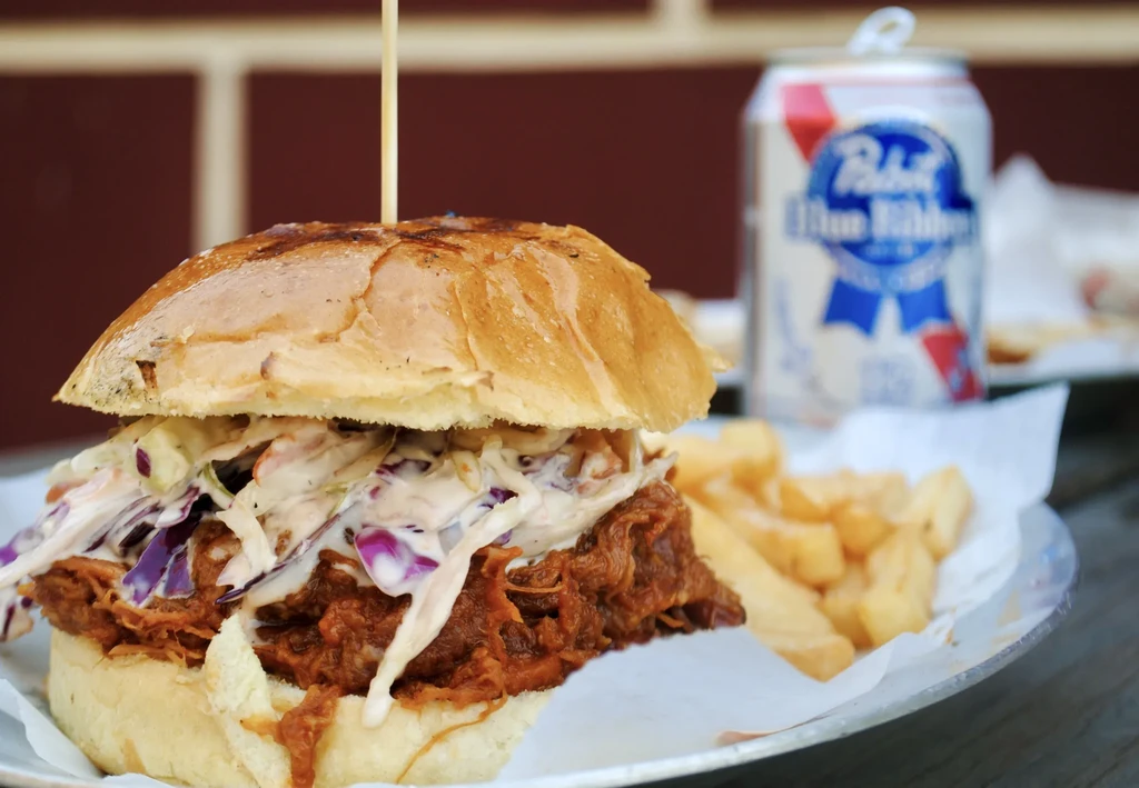 Pulled pork sandwich with coleslaw, fries, and a beer can.