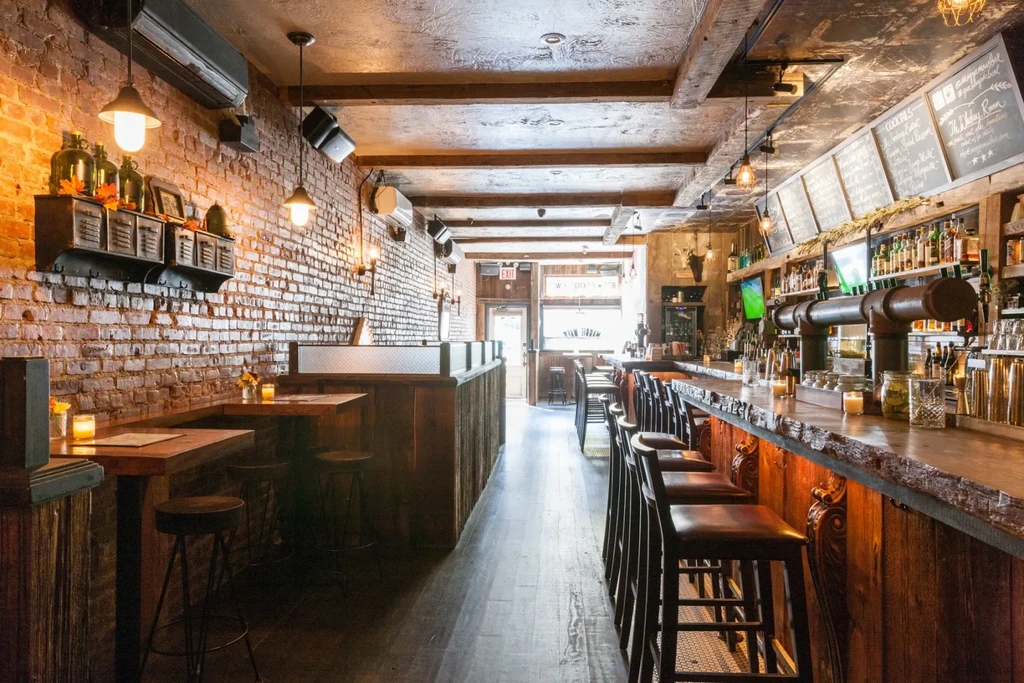 Interior of a bar with brick walls, a wooden bar, and high stools.