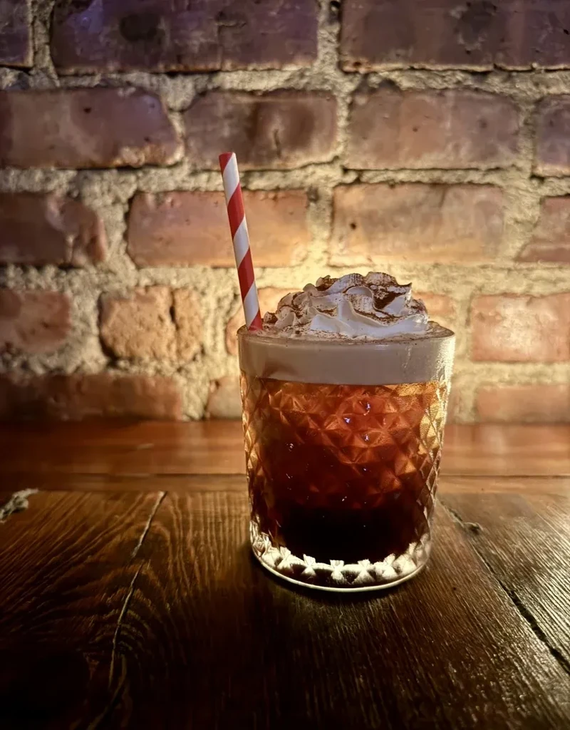 A cocktail with whipped cream, cocoa powder, and a red-striped straw.