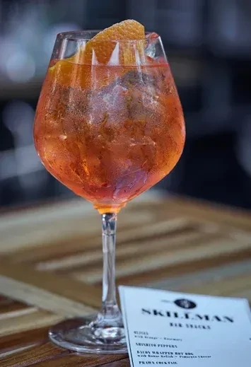 A misty glass of orange spritz with an orange peel garnish.