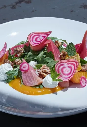 Beet and arugula salad with walnuts and cream on a white plate.