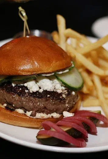A gourmet burger with feta, cucumber, pickled onions, and fries.