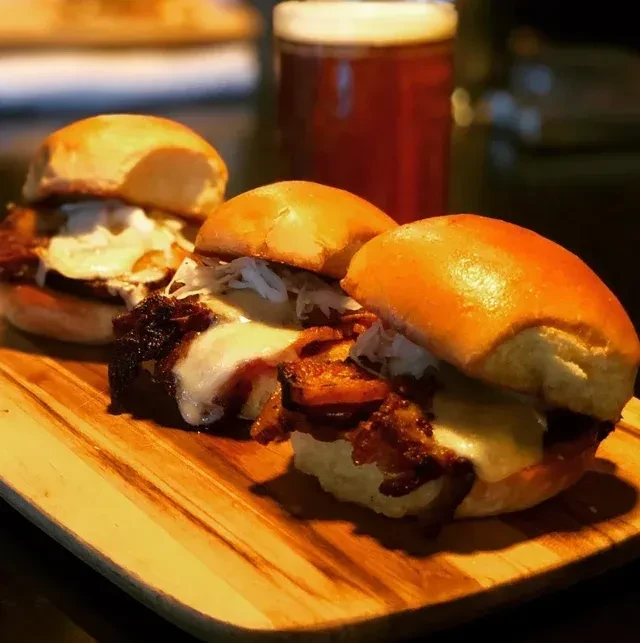 Three sliders with various toppings on a wooden board.