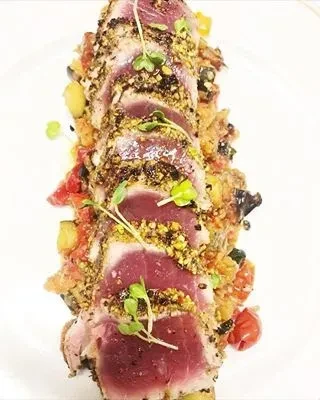 Seared tuna with a seed crust, garnished with sprouts, on a bed of vegetables.