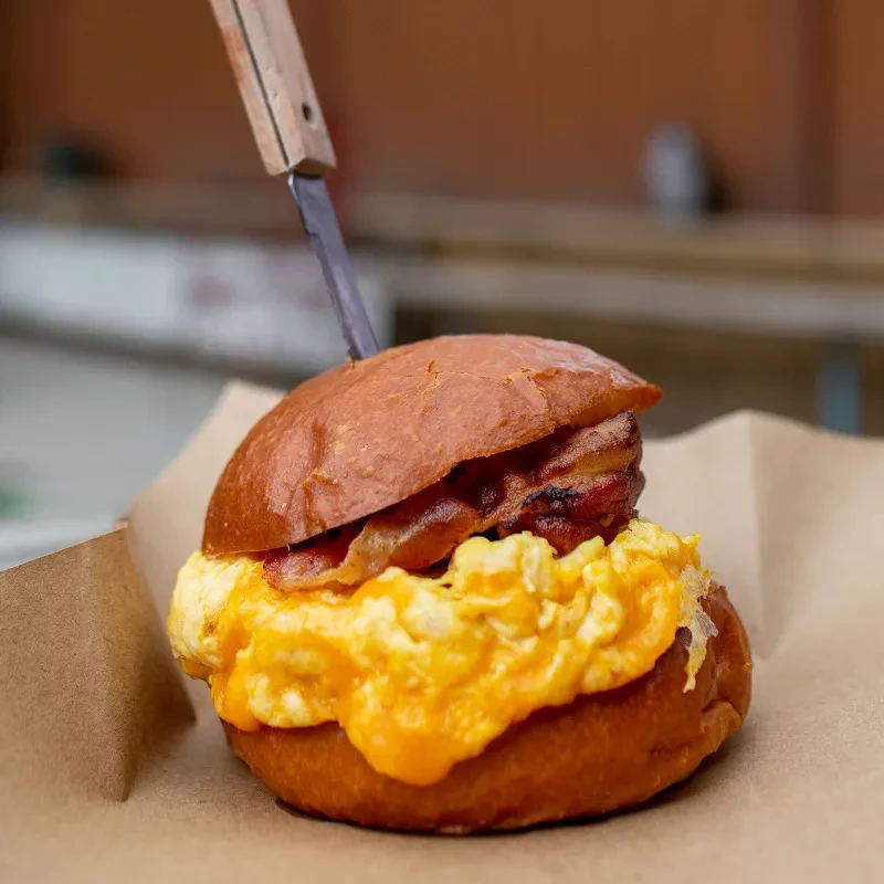 A breakfast sandwich with bacon and scrambled eggs, held by a knife.