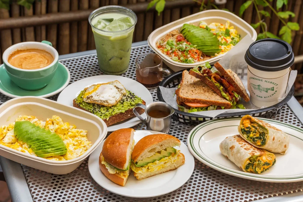 Various breakfast and lunch dishes with beverages on a metal table.