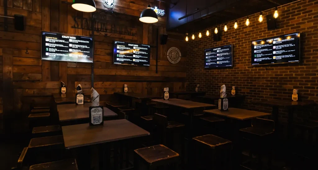 Rustic bar interior with empty tables, brick walls, and digital menus.