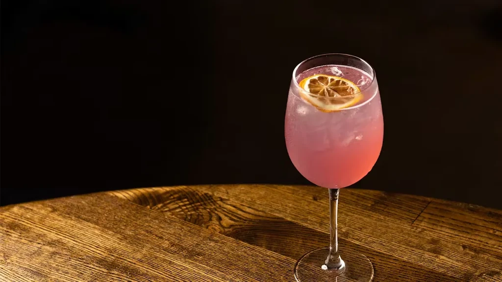 A pink cocktail with an orange slice on a wooden table.
