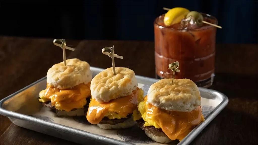 Three breakfast sliders with eggs and cheese on biscuits with a Bloody Mary.