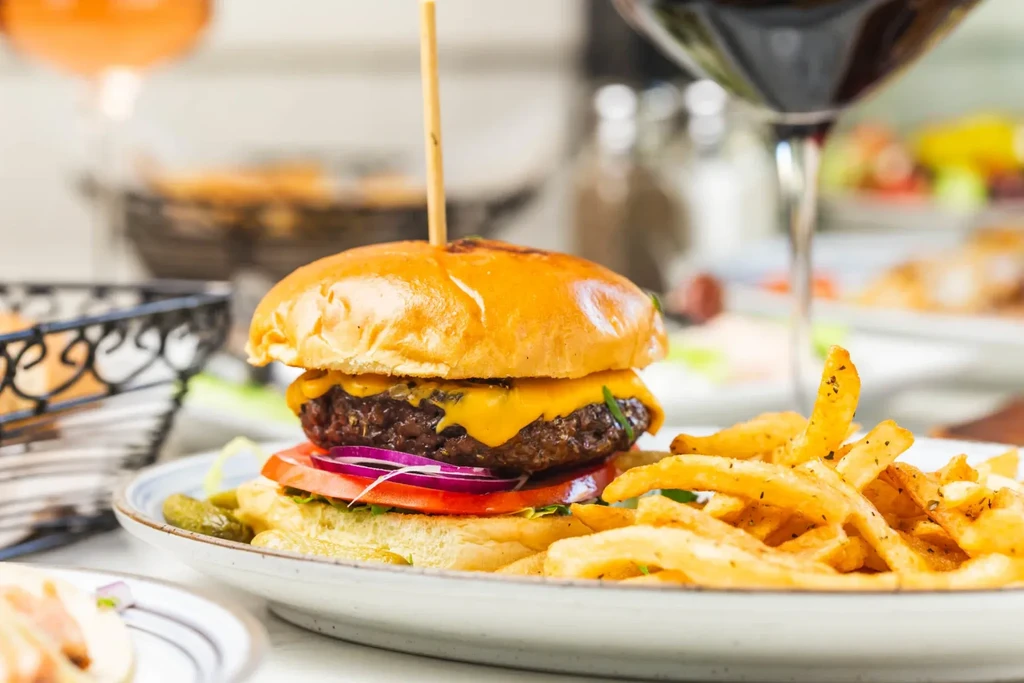 A cheeseburger with fries, pickles, and a glass of red wine.