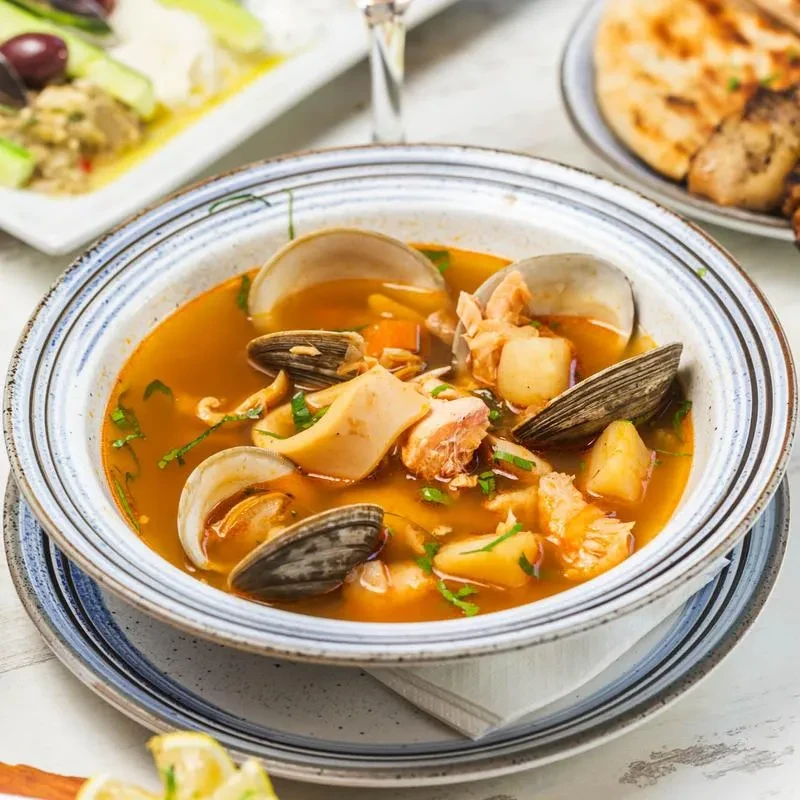 A bowl of seafood soup with clams, fish, and potatoes.