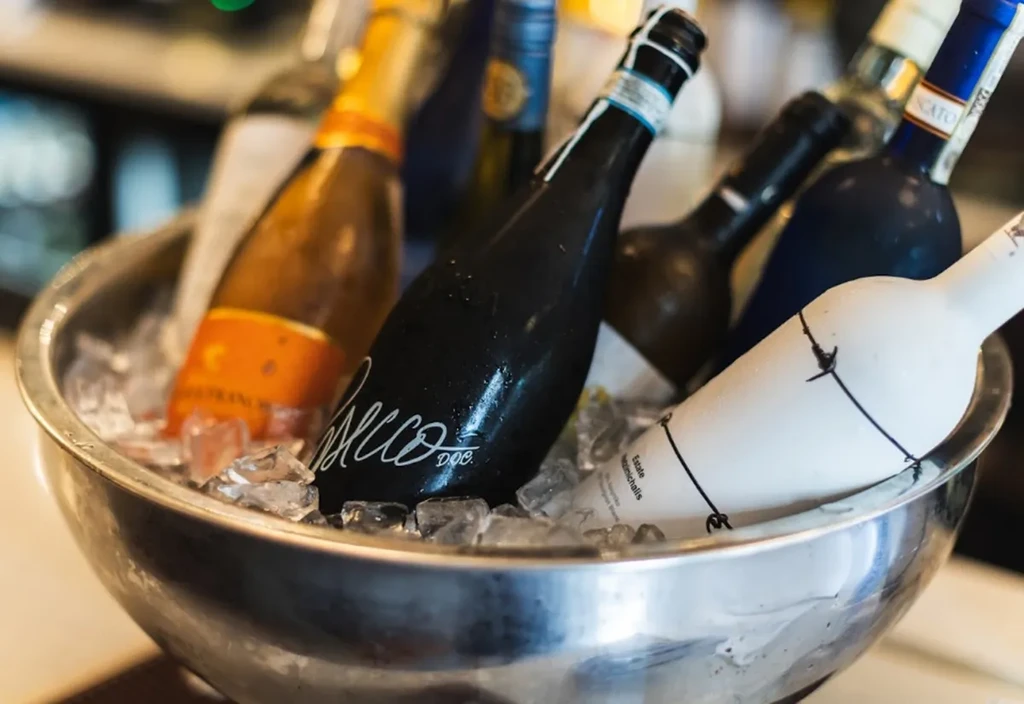 A metal bowl of ice chilling multiple wine bottles.