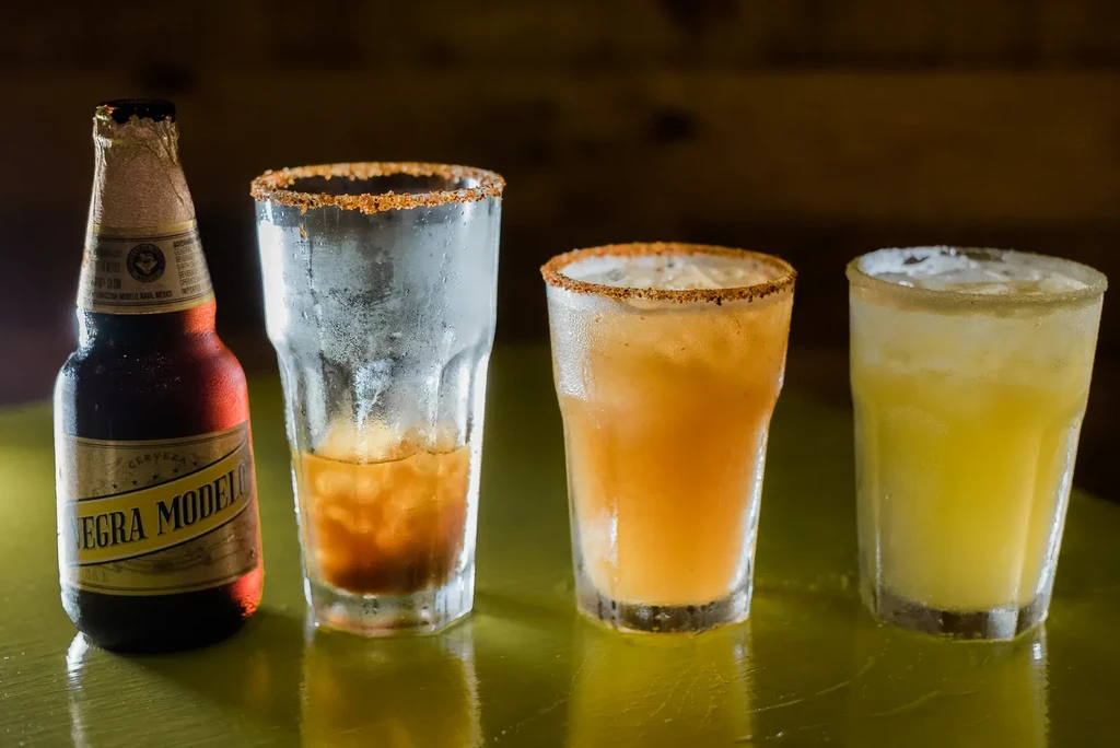 Four cold Mexican beer drinks on a green table.