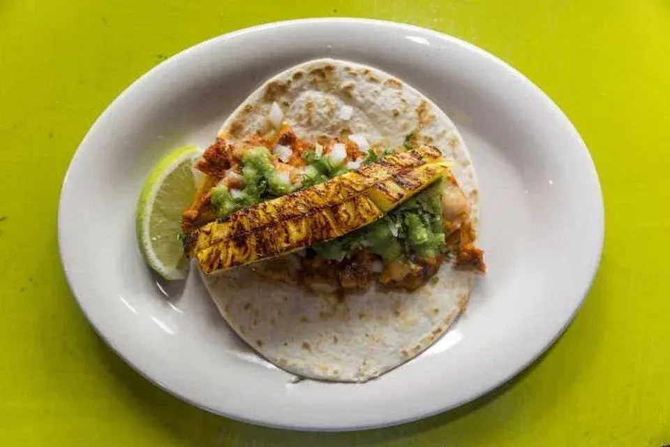 An al pastor taco on a white plate with a lime wedge.