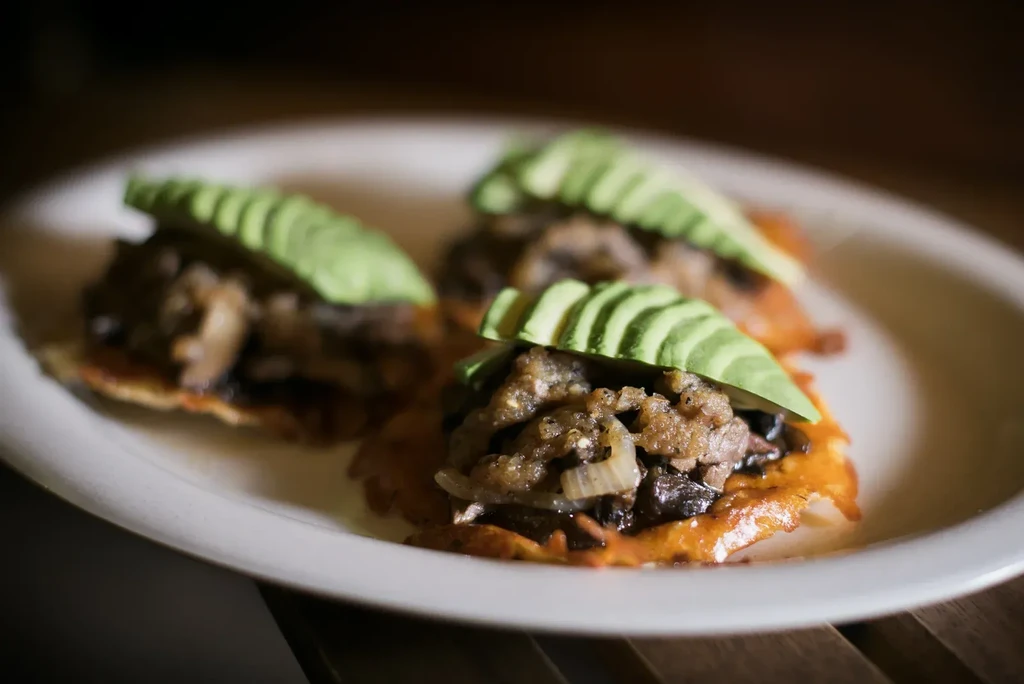Three tostadas topped with mushrooms, onions, and avocado slices.