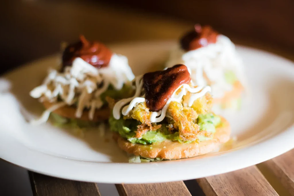 Three sopes topped with various ingredients on a white plate.