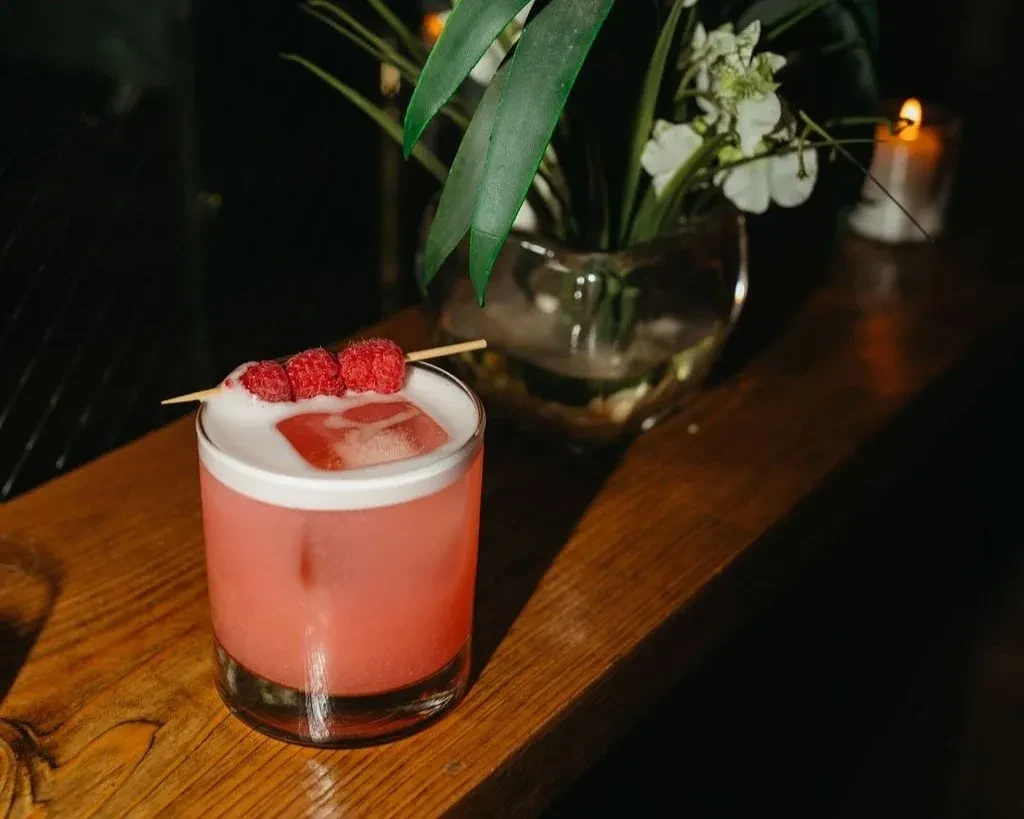 Pink cocktail with raspberries and foam on a wooden table.