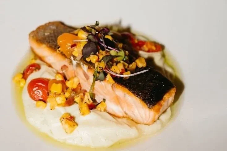 Pan-seared salmon on white purée with corn salsa and microgreens.