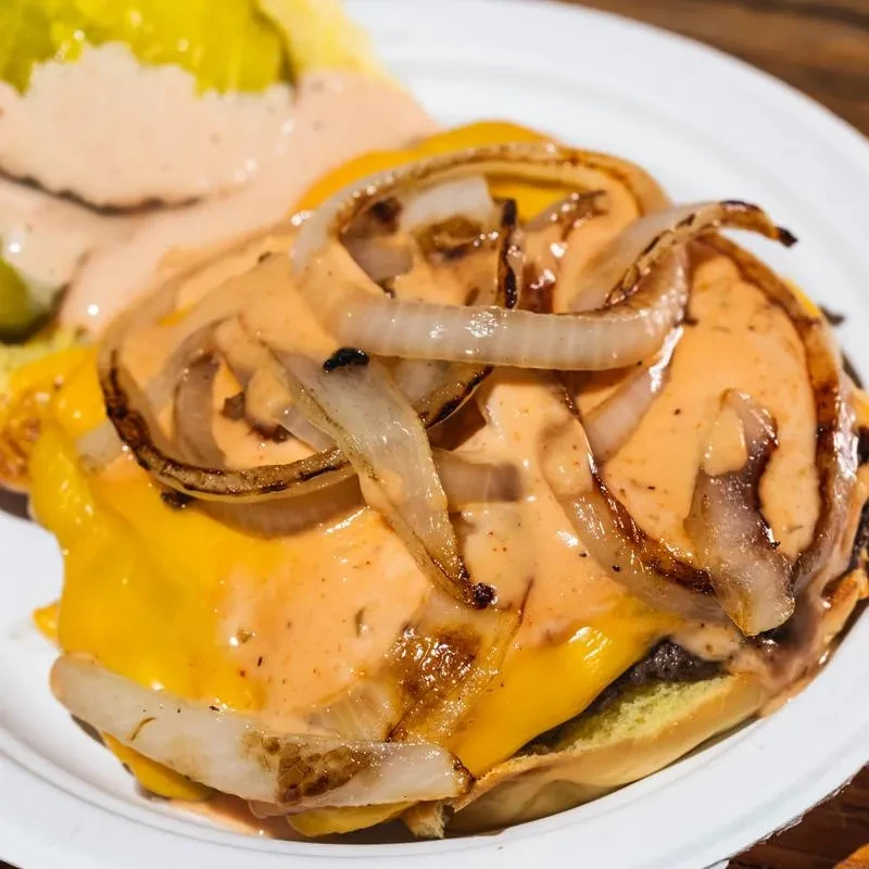 A messy cheeseburger with caramelized onions, sauce, and lettuce on a white plate.