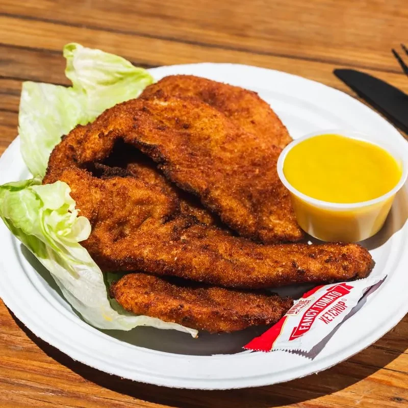 A white plate with fried chicken, lettuce, yellow sauce, and ketchup.