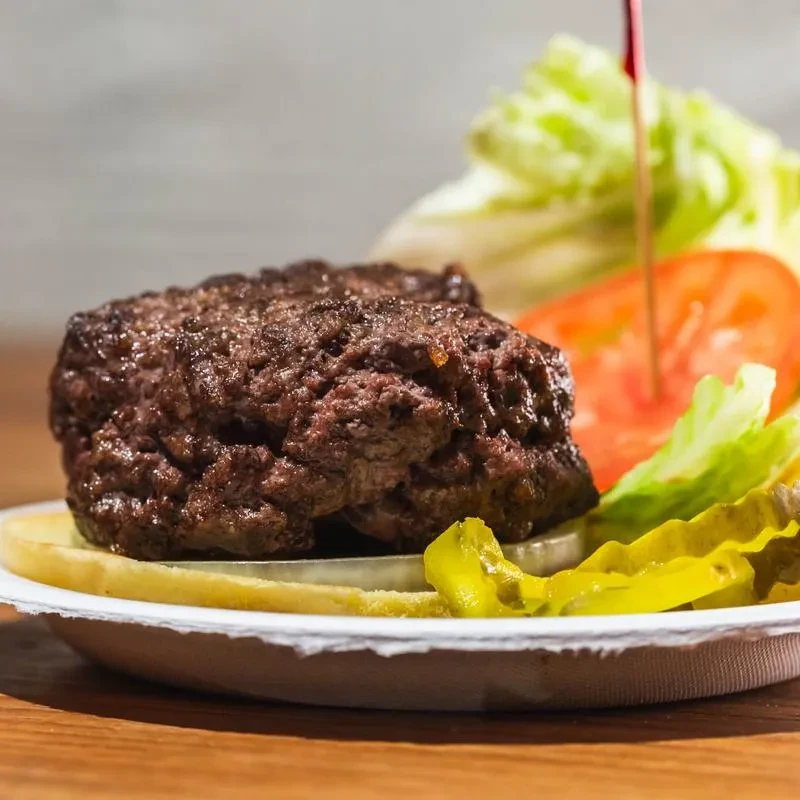 A char-grilled hamburger patty on a bun with toppings on a paper plate.