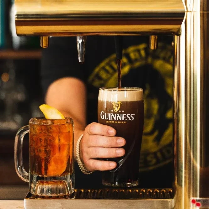 A bartender pours Guinness from a golden tap into a branded glass.