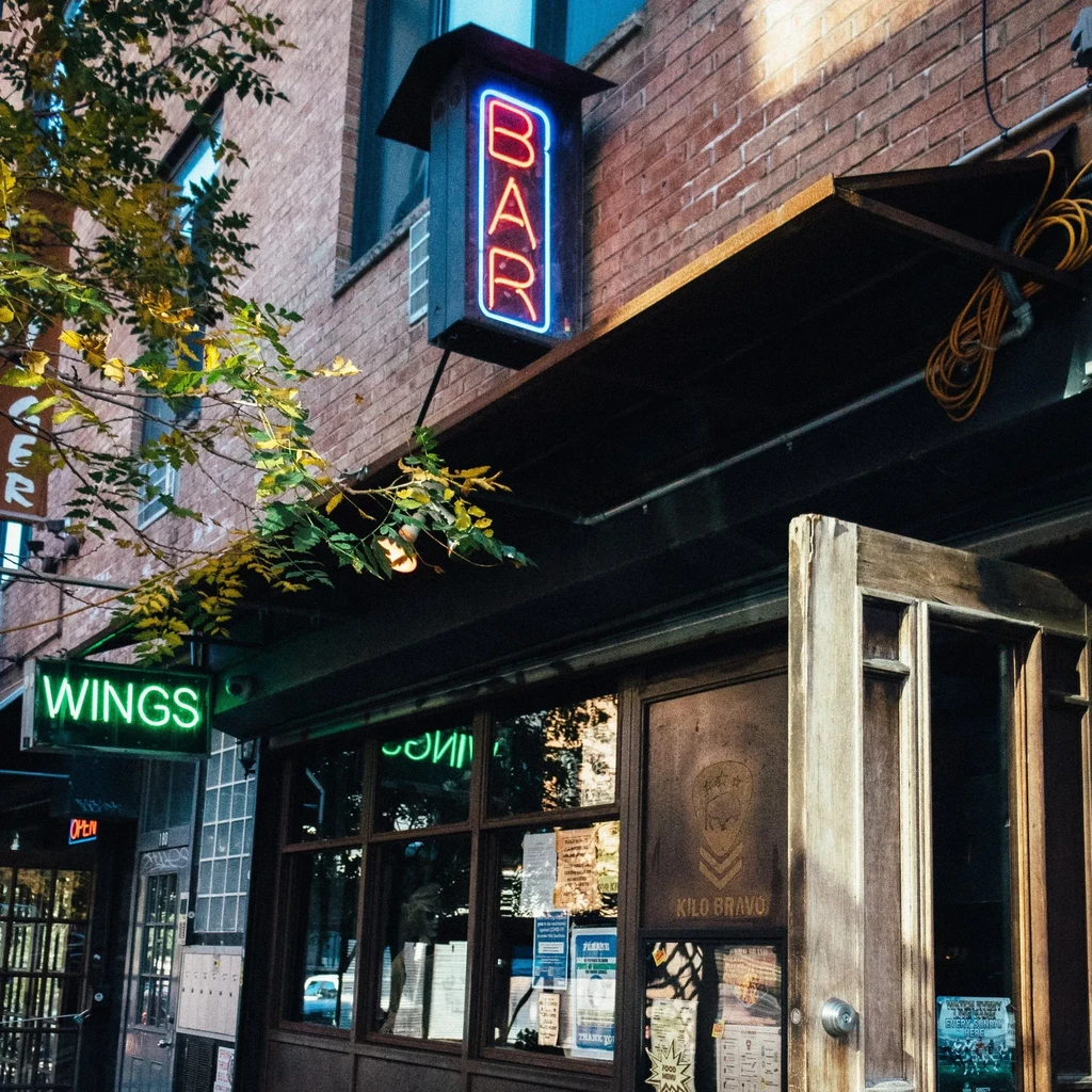 Neon "BAR" and "WINGS" signs on a brick building facade.