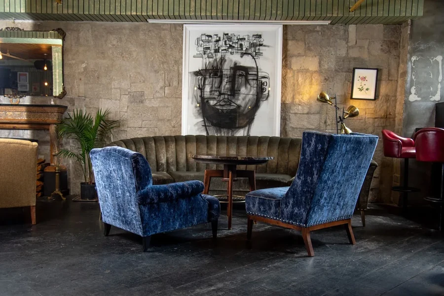 Lounge room with blue velvet chairs, olive sofa, and abstract art.