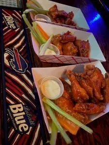 Three plates of chicken wings, celery, carrots, and dip with a Labatt Blue mat.