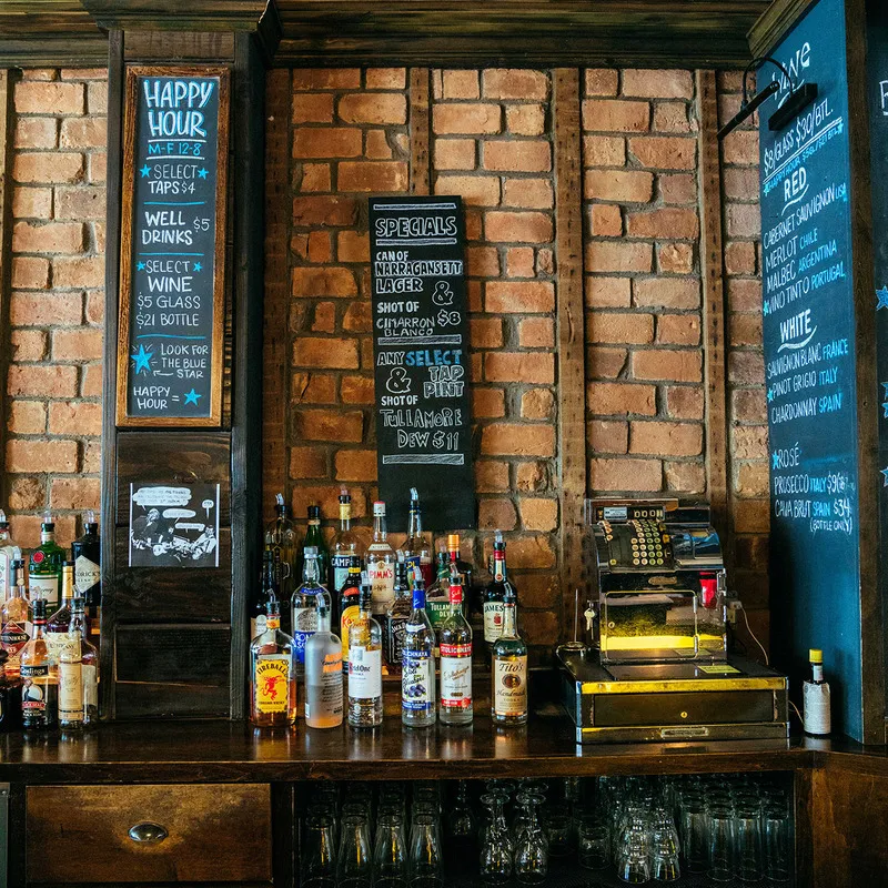 Bar counter with liquor bottles, three menu boards, and brick wall.