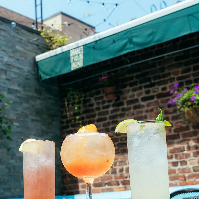 Three cocktails sit on a table against a brick wall and green awning.