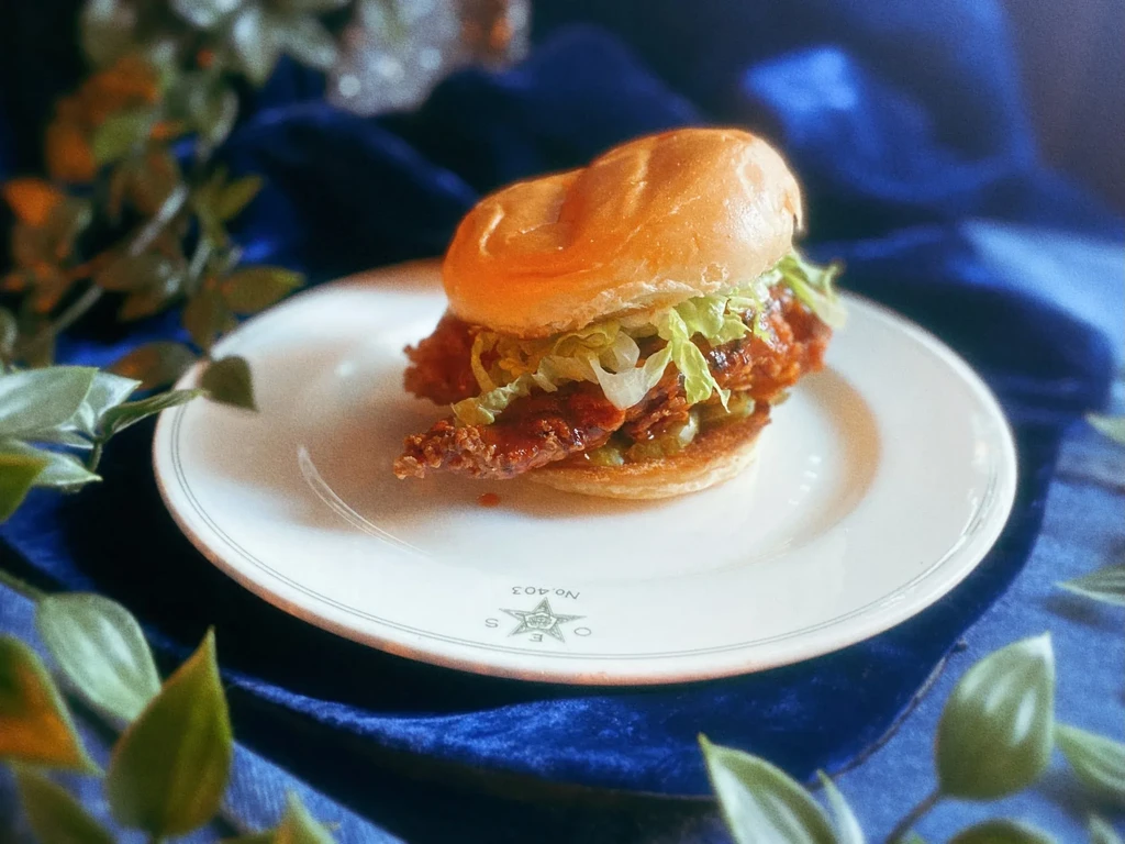 A fried chicken sandwich on a white plate with blue and green accents.