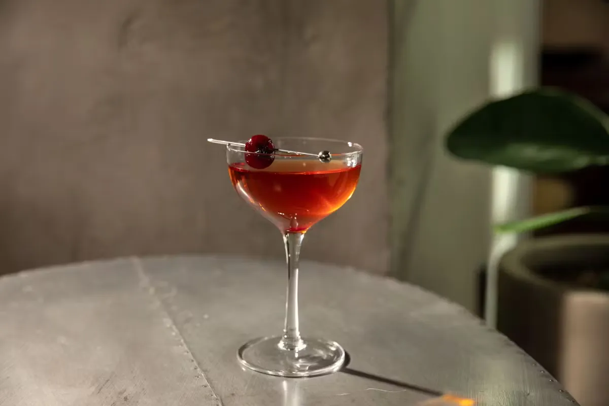 Red cocktail with a cherry garnish on a metal table.