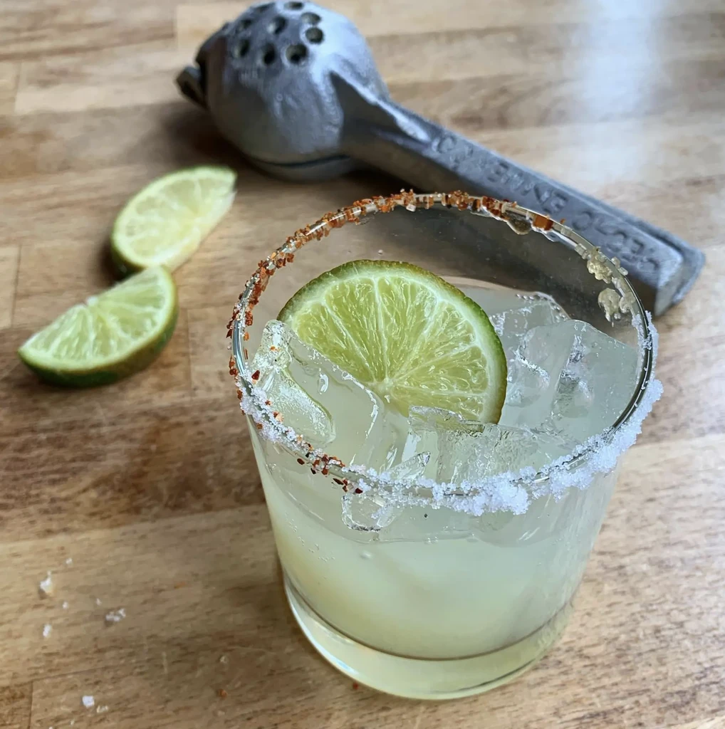 Margarita with lime wedge and salt rim, citrus press, and lime slices.