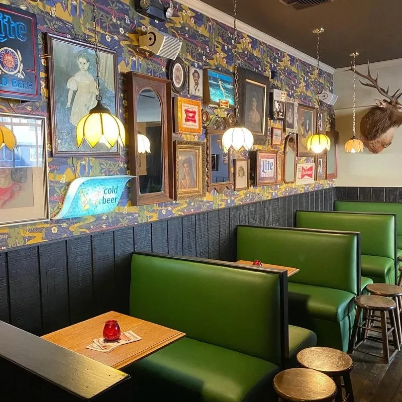 A quirky bar or restaurant with green booths, eclectic framed art, and deer head.