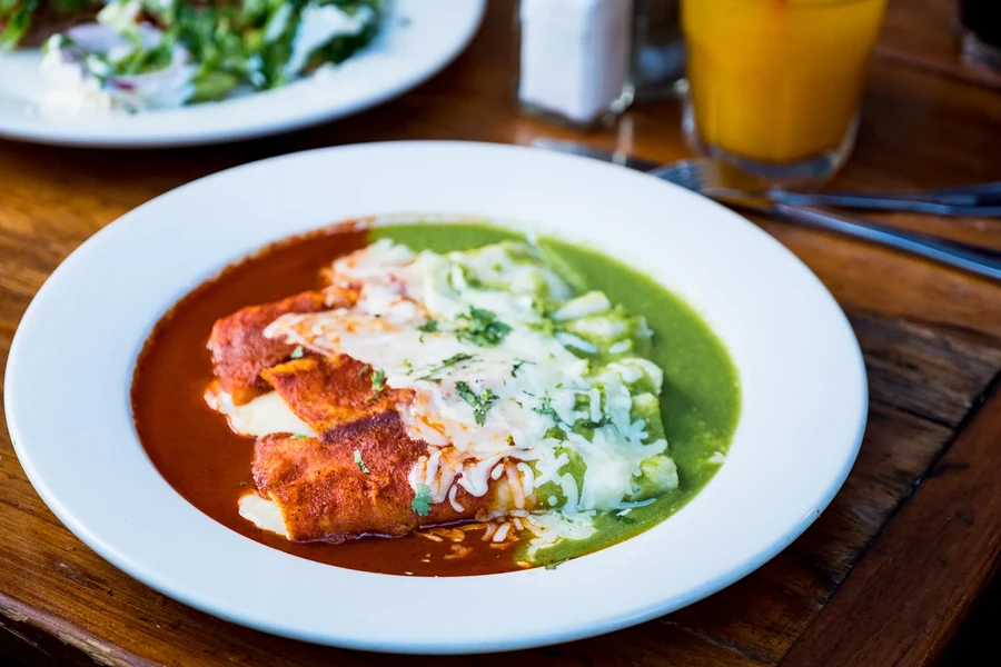A plate of enchiladas with red and green sauce, topped with cheese.