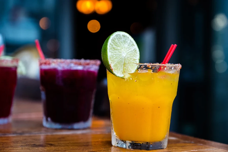 Two fruit drinks with salted rims and straws on a wooden table.