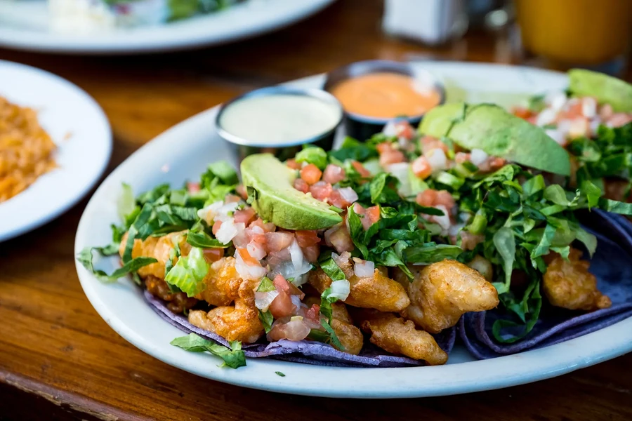 A plate of fish tacos with avocado, salsa, and shredded lettuce.