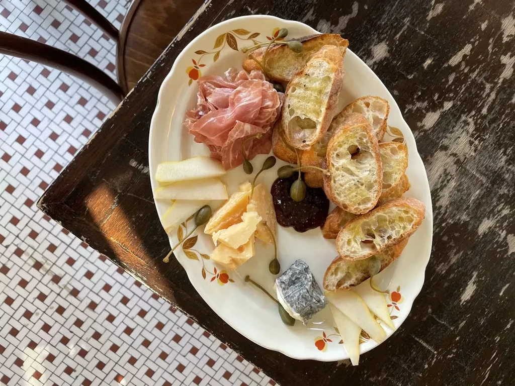 Charcuterie board with prosciutto, cheese, bread, fruit, and caper berries.