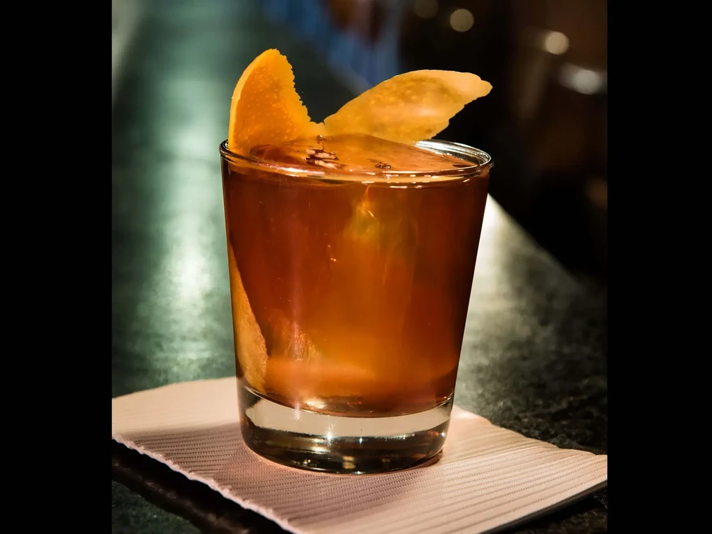 A short glass of amber liquid with an orange peel and chip garnish.